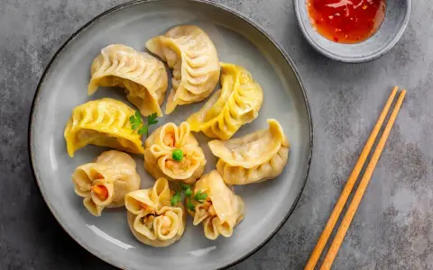 Talerz pełen aromatycznych chińskich pierożków, gotowych do zanurzenia w sosie. Obok pałeczki i miseczka z ostrym dipem.