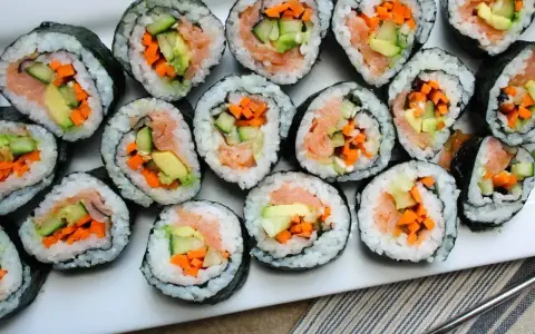 Ułożone na talerzu rolki sushi z łososiem, awokado, ogórkiem i marchewką. Widać, co do sushi do środka, czyli świeże składniki.