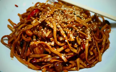 Makaron chow mein z sezamem i papryką na białym talerzu, z pałeczkami.