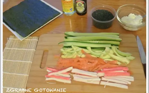 Pokrojone składniki do sushi: ogórek, łosoś, paluszki krabowe, awokado, sezam, sos sojowy, ryż i nori.