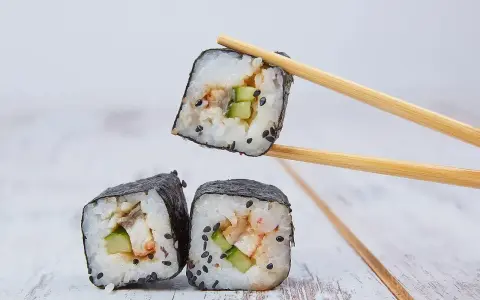 Trzy kawałki sushi z ryżem, ogórkiem i rybą, jeden podniesiony pałeczkami. Idealne do sosu sojowego, czyli zalewa do sushi.