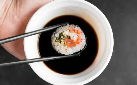 Pałeczkami zanurzam sushi w sosie kabayaki.