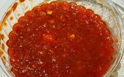 Gęsty, czerwony sos sambal w przezroczystym pojemniku, z widocznymi kawałkami papryczek chili i przypraw.