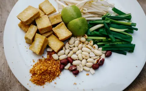 Talerz z pokrojonym tofu, orzeszkami ziemnymi, szczypiorkiem, kiełkami fasoli mung, limonkami i płatkami chili.