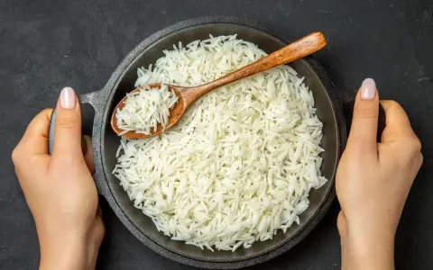 Sypki ryż basmati w misce, nabierany drewnianą łyżką, trzymany przez dwie dłonie.