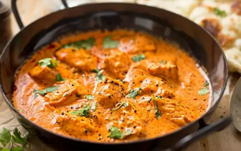 Aksamitny kurczak w sosie curry, udekorowany świeżą kolendrą, kusi aromatem. Obok widać kawałki chleba naan.