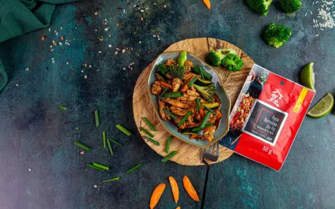 Aksamitny kurczak po kantońsku z brokułami i marchewką, gotowy do podania. Obok paczka pasty do stir-fry.
