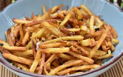 Chrupiące frytki po wietnamsku, posypane skórką limonki i solą, podane w niebieskiej misce.