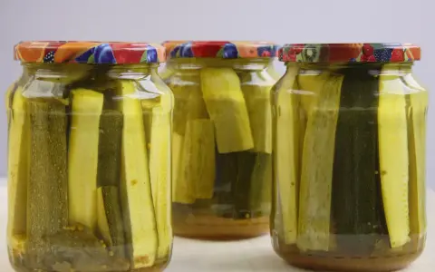 Słoiki z cukinią w zalewie słodko-kwaśnej z curry. Zioła i przyprawy dodają smaku.