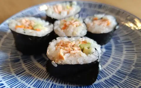Pięć kawałków sushi z łososiem, ryżem i warzywami na niebiesko-białym talerzu.