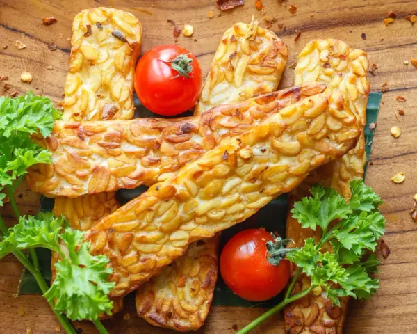 Złociste kawałki tempeh, smażone na złoto, z pomidorkami i natką pietruszki. Tempeh co to? To pyszna, roślinna alternatywa.