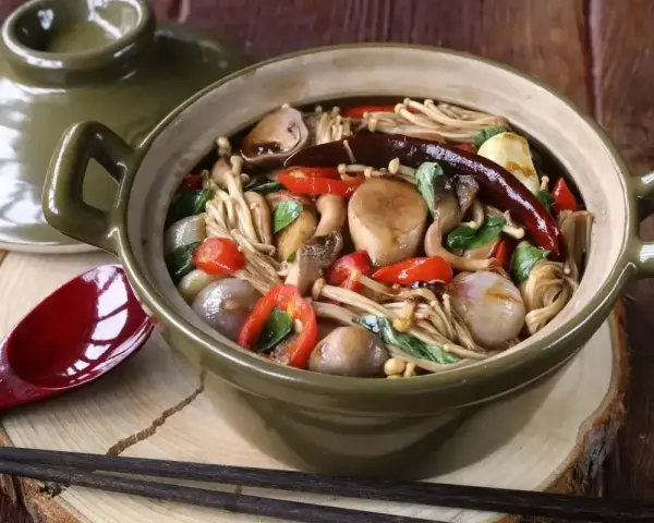 Gęsta zupa z grzybkami mun, papryczkami chili i innymi warzywami w glinianym garnku.