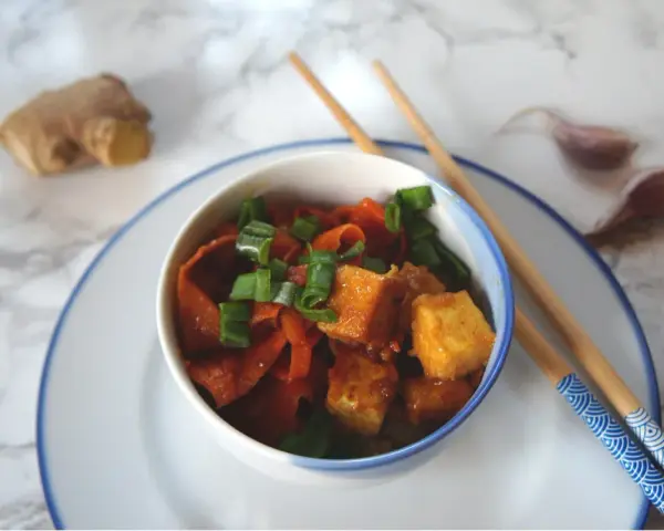 Pyszne dania z tofu z marchewką i szczypiorkiem, gotowe do jedzenia pałeczkami. Obok imbir i czosnek.