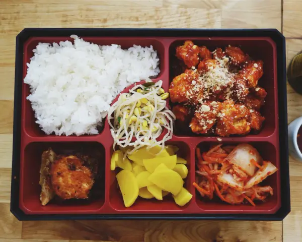 Bento box z ryżem, kurczakiem w sosie, kimchi, fasolką i żółtą rzodkiewką.