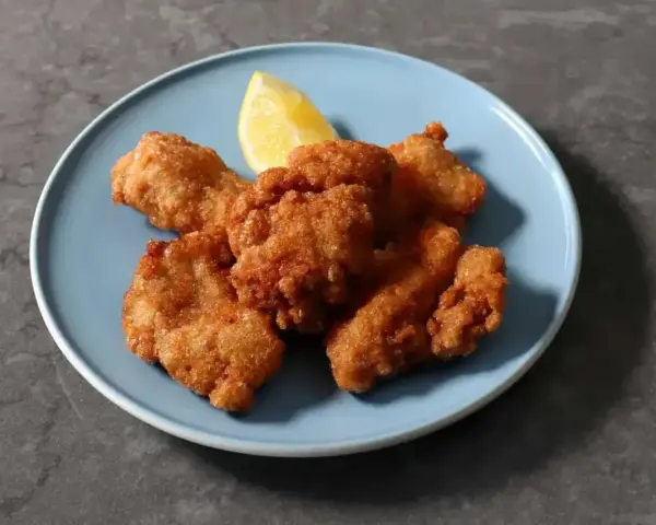 Chrupiące kawałki karaage, złociste i apetyczne, podane z ćwiartką cytryny na niebieskim talerzu.