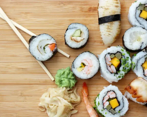 Różnorodne sushi z krewetkami, mango i warzywami, pałeczki, wasabi i marynowany imbir na drewnianym tle.