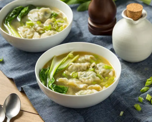 Dwie miseczki aromatycznej zupy won ton z zielonymi warzywami i posiekanym szczypiorkiem.