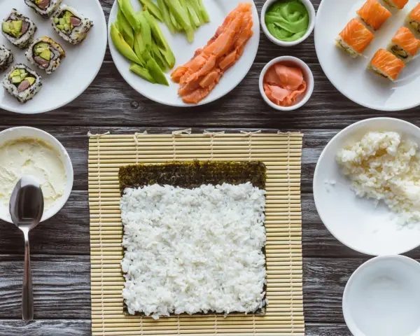 Przygotowanie sushi: ryż, nori, łosoś, awokado, wasabi i marynowany imbir na drewnianym blacie.