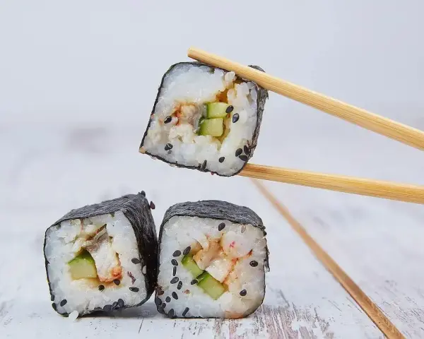 Trzy kawałki sushi z ryżem, ogórkiem i rybą, jeden podniesiony pałeczkami. Idealne do sosu sojowego, czyli zalewa do sushi.