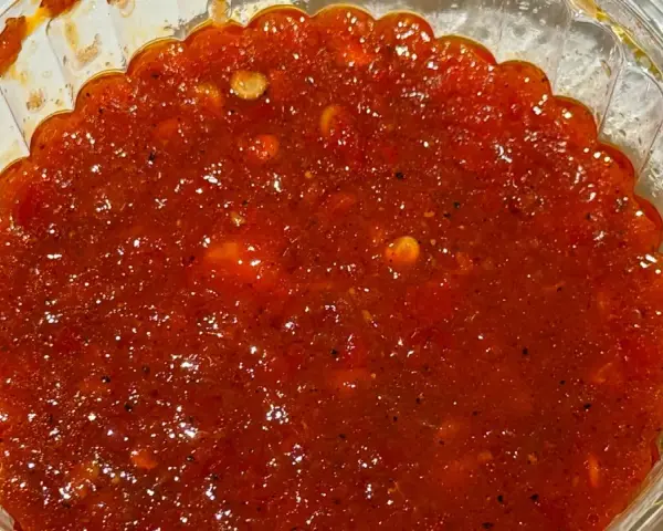 Gęsty, czerwony sos sambal w przezroczystym pojemniku, z widocznymi kawałkami papryczek chili i przypraw.
