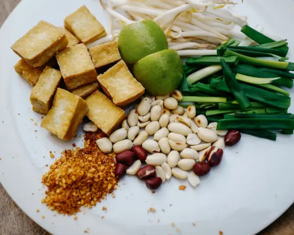 Talerz z pokrojonym tofu, orzeszkami ziemnymi, szczypiorkiem, kiełkami fasoli mung, limonkami i płatkami chili.