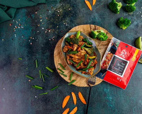 Aksamitny kurczak po kantońsku z brokułami i marchewką, gotowy do podania. Obok paczka pasty do stir-fry.
