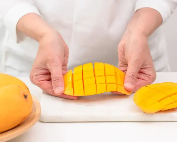 Ręce trzymają pokrojonego w kostkę mango. Ten soczysty owoc jest gotowy do jedzenia.