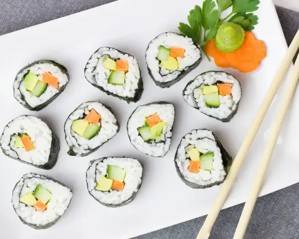 Smaczne futomaki z awokado, ogórkiem i marchewką, udekorowane natką pietruszki i wasabi.