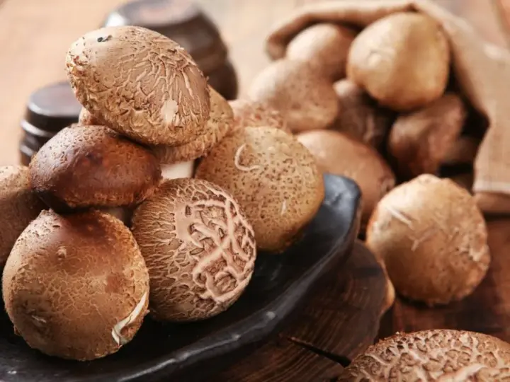 Kupa świeżych grzybów shiitake na czarnej desce, niektóre w worku jutowym.