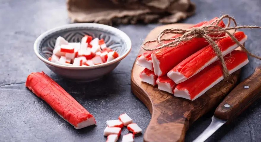 Surimi co to? Paluszki krabowe, pokrojone i całe, na desce i w miseczce, gotowe do sałatki.