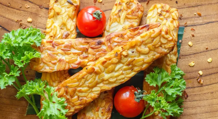Złociste kawałki tempeh, smażone na złoto, z pomidorkami i natką pietruszki. Tempeh co to? To pyszna, roślinna alternatywa.