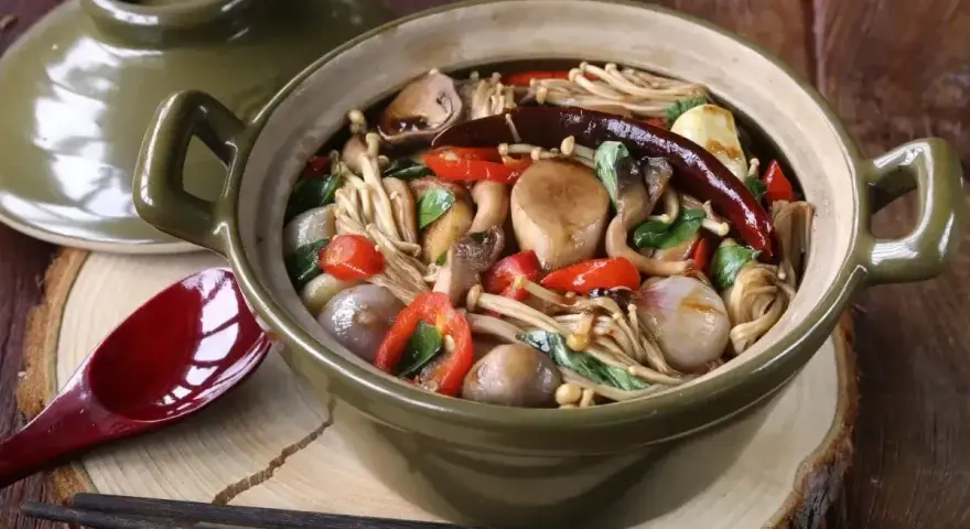 Gęsta zupa z grzybkami mun, papryczkami chili i innymi warzywami w glinianym garnku.