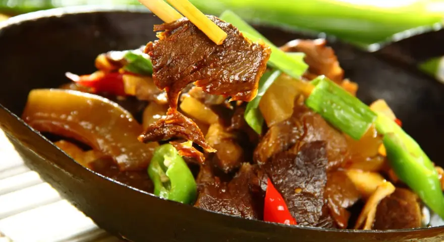 Chopsticks podnoszą kawałek aromatycznej wołowiny po chińsku z miski pełnej pysznego dania z warzywami.