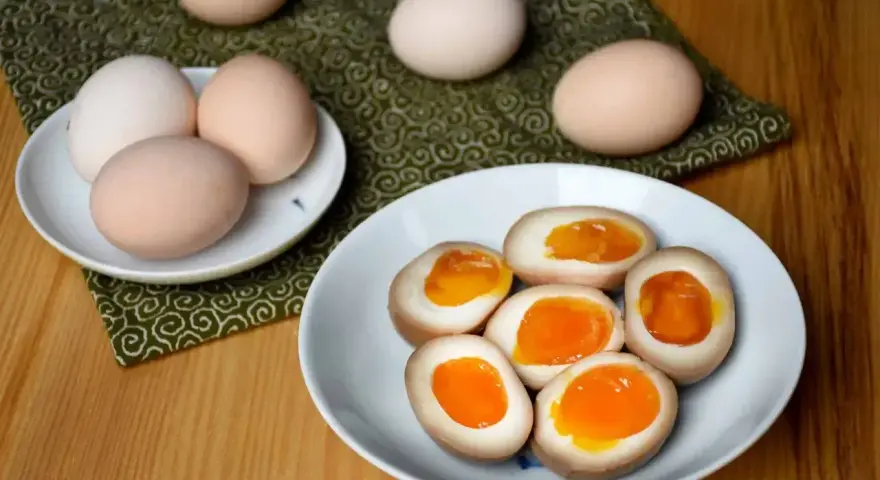 Na talerzu leżą połówki jajek do ramenu z płynnym, pomarańczowym żółtkiem. Obok całe jajka.