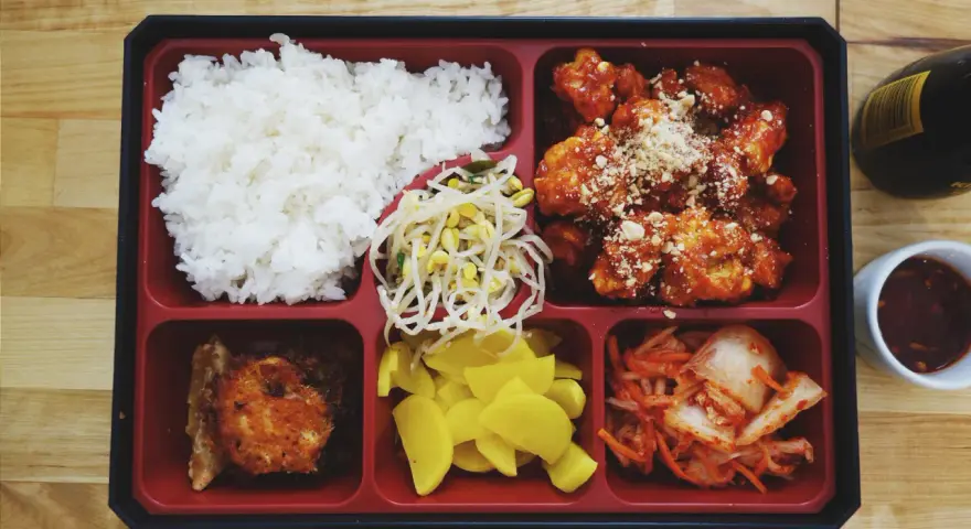 Bento box z ryżem, kurczakiem w sosie, kimchi, fasolką i żółtą rzodkiewką.