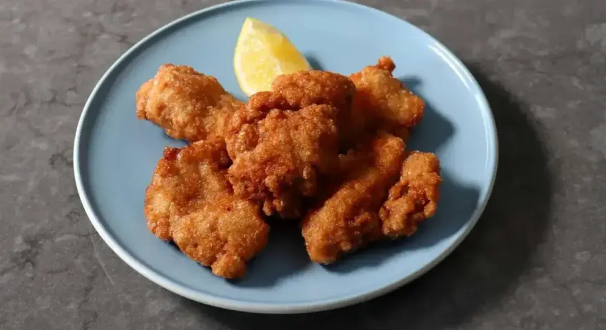 Chrupiące kawałki karaage, złociste i apetyczne, podane z ćwiartką cytryny na niebieskim talerzu.