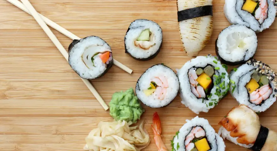 Różnorodne sushi z krewetkami, mango i warzywami, pałeczki, wasabi i marynowany imbir na drewnianym tle.
