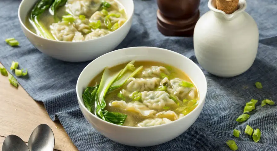 Dwie miseczki aromatycznej zupy won ton z zielonymi warzywami i posiekanym szczypiorkiem.