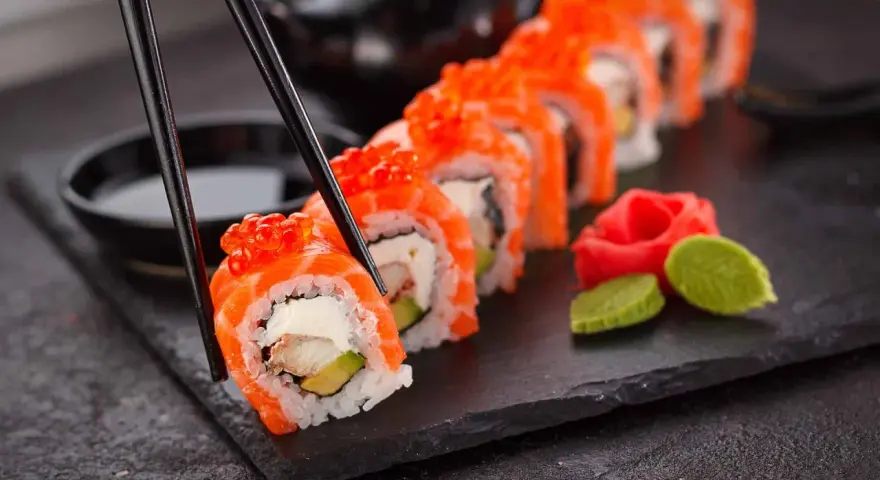 Chopsticks podnoszą kawałek sushi z łososiem i ikrą. Czy sushi jest lekkostrawne? Zależy od składników, ale to wygląda apetycznie.