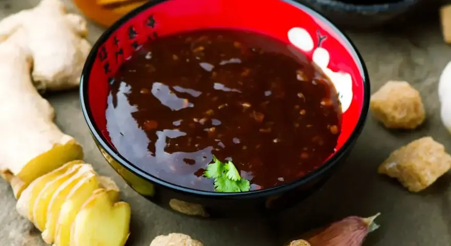 Miseczka z aromatycznym sosem teriyaki, obok świeży imbir, czosnek i brązowy cukier.