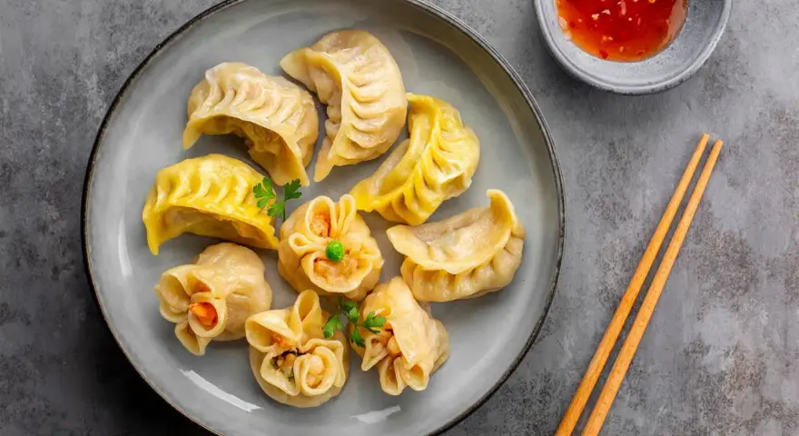 Talerz pełen aromatycznych chińskich pierożków, gotowych do zanurzenia w sosie. Obok pałeczki i miseczka z ostrym dipem.