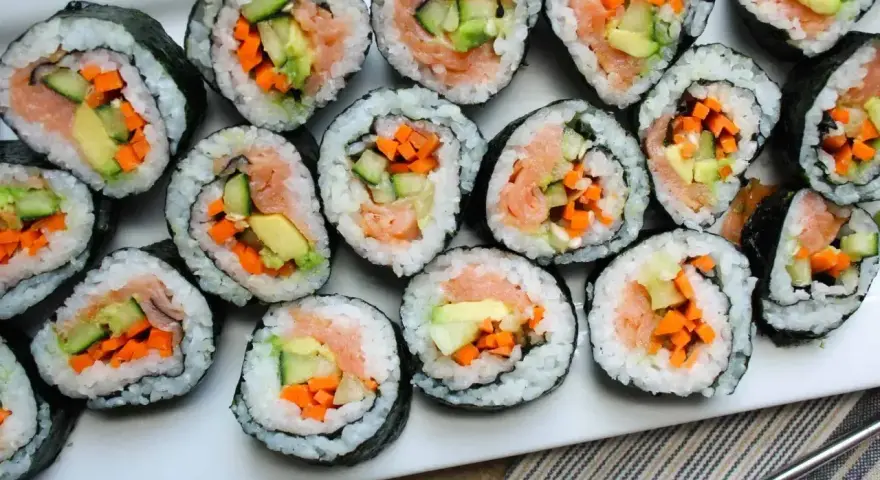 Ułożone na talerzu rolki sushi z łososiem, awokado, ogórkiem i marchewką. Widać, co do sushi do środka, czyli świeże składniki.