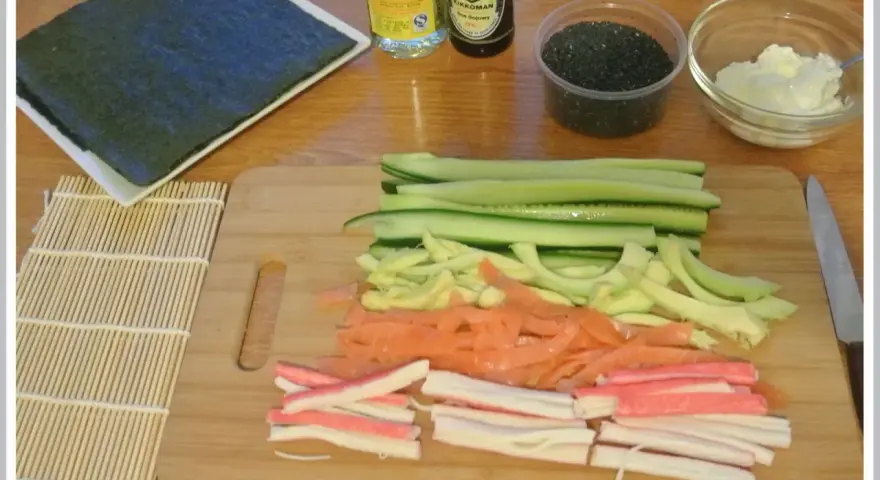 Pokrojone składniki do sushi: ogórek, łosoś, paluszki krabowe, awokado, sezam, sos sojowy, ryż i nori.