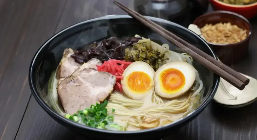 Parujący ramen: makaron, plastry wieprzowiny, jajko na pół, szczypiorek i grzyby. Pyszne danie, które rozgrzewa.
