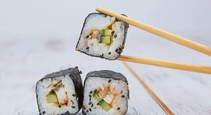 Trzy kawałki sushi z ryżem, ogórkiem i rybą, jeden podniesiony pałeczkami. Idealne do sosu sojowego, czyli zalewa do sushi.