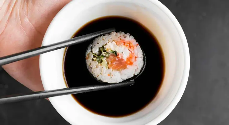 Pałeczkami zanurzam sushi w sosie kabayaki.