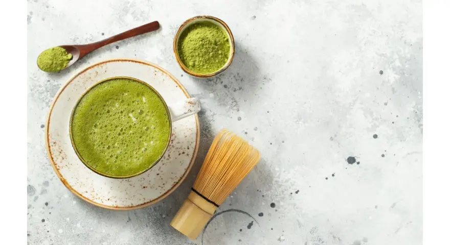 Zielona, spieniona matcha w filiżance, obok bambusowa miotełka i łyżeczka z proszkiem. To właśnie co to matcha – napój pełen energii.