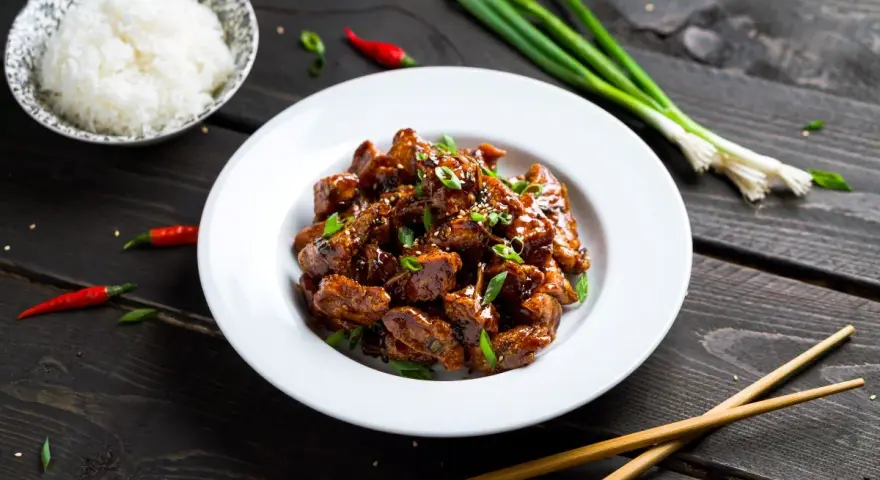 Pyszny kurczak po sajgońsku w sosie, posypany szczypiorkiem i sezamem, obok miseczka ryżu, pałeczki i papryczki chili.