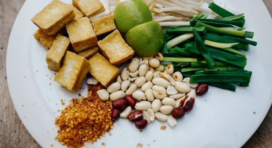 Talerz z pokrojonym tofu, orzeszkami ziemnymi, szczypiorkiem, kiełkami fasoli mung, limonkami i płatkami chili.