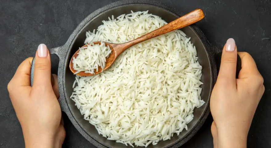 Sypki ryż basmati w misce, nabierany drewnianą łyżką, trzymany przez dwie dłonie.